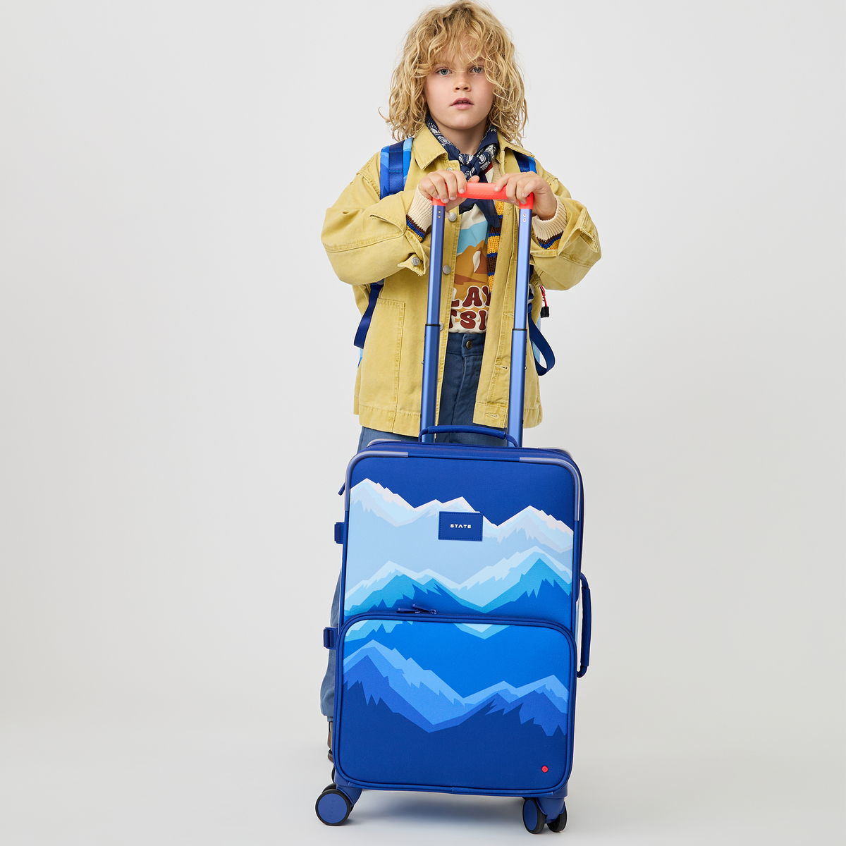 boy holding STATE Bags Logan Carry-On Suitcase MOuntains 