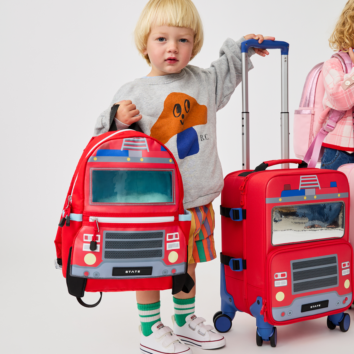 boy holding STATE Bags Mini Logan Carry-On Suitcase Firetruck 